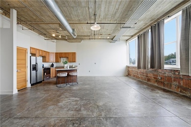 Kitchen with stainless steel appliances, light countertops, a kitchen island, concrete flooring, and brown cabinetry