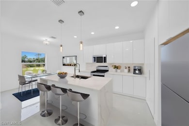 Kitchen featuring appliances with stainless steel finishes, sink, hanging light fixtures, decorative backsplash, and white cabinetry