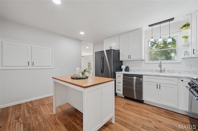 Kitchen featuring white hardward adorned cabinets, simply stated backsplash, pendant lighting, butcher block countertops, and recessed lighting