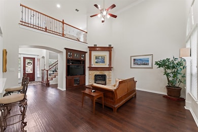 Living area featuring a stone fireplace, a ceiling fan, a towering ceiling, arched walkways, and stairs