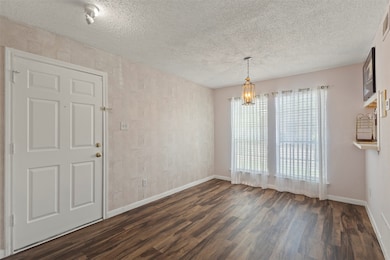 Unfurnished dining area featuring dark wood-style floors, a textured ceiling, and a chandelier