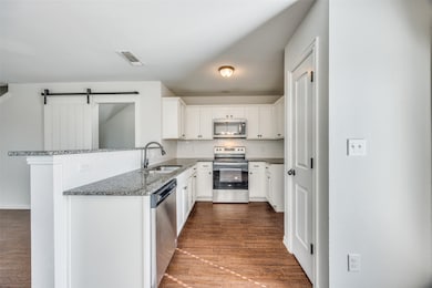 Kitchen featuring a barn door, decorative backsplash, appliances with stainless steel finishes, dark wood-style floors, and a peninsula