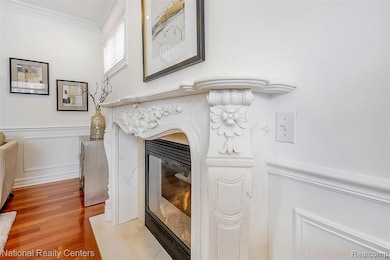 Detailed view of crown molding, a fireplace, wood finished floors, wainscoting, and a decorative wall