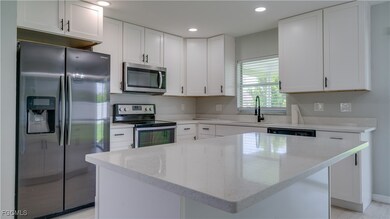 Kitchen featuring stainless steel appliances, white cabinetry, light stone counters, a kitchen island, and recessed lighting