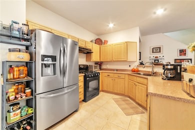 Kitchen with stainless steel fridge, black gas range oven, light brown cabinets, light countertops, and light tile patterned floors
