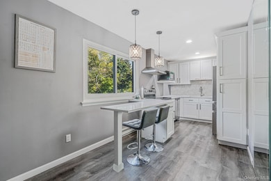 Kitchen with a breakfast bar, tasteful backsplash, hanging light fixtures, dark wood-type flooring, and wall chimney range hood