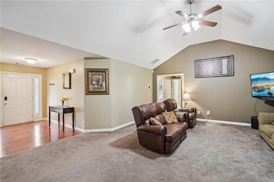 Carpeted living room with ceiling fan and lofted ceiling
