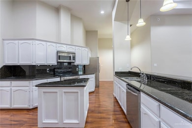 Kitchen with appliances with stainless steel finishes, white cabinetry, dark wood finished floors, and backsplash