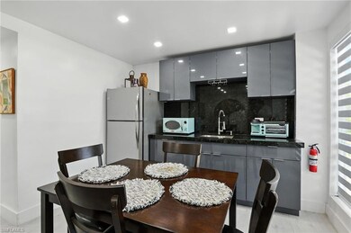 Kitchen with modern gray cabinetry, granite counters and backsplash, freestanding refrigerator, and recessed lighting