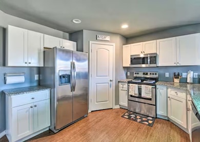 Kitchen featuring appliances with stainless steel finishes, light stone counters, white cabinetry, light wood-type flooring, and recessed lighting