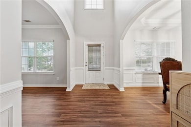 Foyer featuring crown molding, wood finished floors, a wainscoted wall, and arched walkways