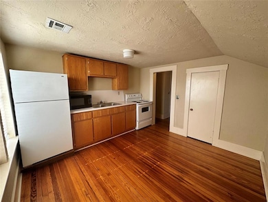 Kitchen with white appliances, a sink, dark wood-style flooring, light countertops, and brown cabinetry