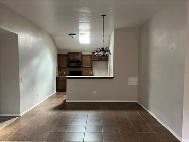 Kitchen with black microwave, backsplash, dark tile patterned floors, a chandelier, and pendant lighting
