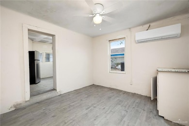 Empty room with a wall mounted air conditioner, wood finished floors, and a ceiling fan
