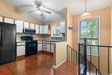 Kitchen featuring black appliances, a sink, white cabinets, lofted ceiling, and dark wood finished floors