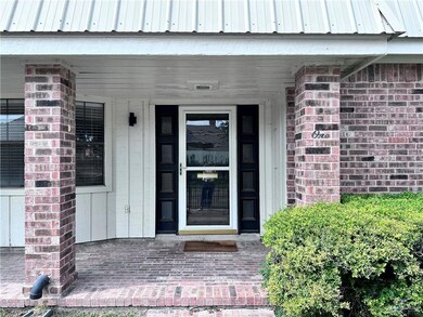 Entrance to property featuring covered porch, brick siding, and metal roof