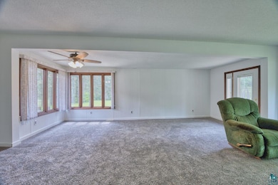 Unfurnished living room with a ceiling fan, carpet flooring, a textured ceiling, and baseboards