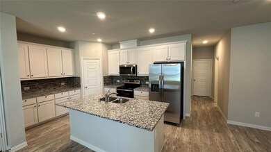Kitchen with white cabinets, a center island with sink, appliances with stainless steel finishes, and light hardwood / wood-style flooring