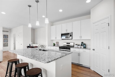 Kitchen featuring a kitchen bar, appliances with stainless steel finishes, recessed lighting, light wood-style flooring, and an island with sink