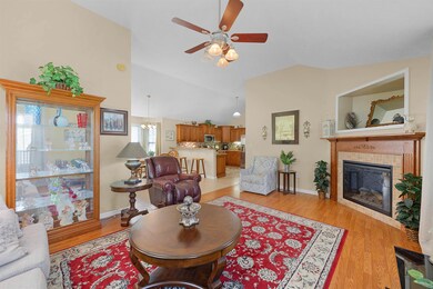 Living area featuring ceiling fan, a fireplace, vaulted ceiling, baseboards, and light wood-style floors
