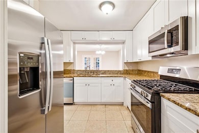 Kitchen with appliances with stainless steel finishes, white cabinetry, and light stone countertops