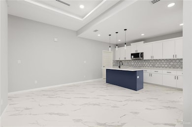 Kitchen with backsplash, sink, decorative light fixtures, a center island with sink, and white cabinets