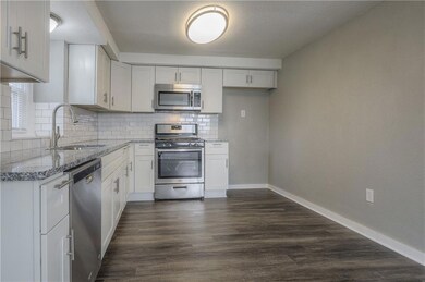 Kitchen with stainless steel appliances, light stone countertops, tasteful backsplash, white cabinets, and dark wood-type flooring