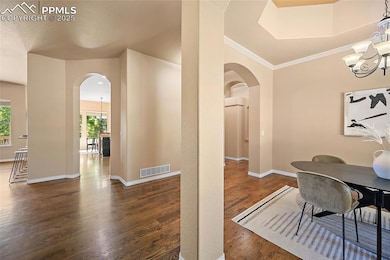 Dining room featuring arched walkways, a chandelier, plenty of natural light, wood finished floors, and ornamental molding