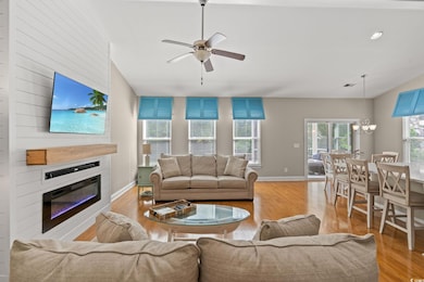 Living room with light wood-style floors, a fireplace, ceiling fan, a chandelier, and vaulted ceiling