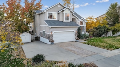 Traditional home featuring a garage, stucco siding, a storage unit, a shingled roof, and driveway