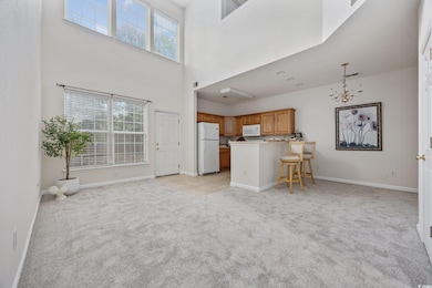 Living room with light colored carpet, a chandelier, and a towering ceiling