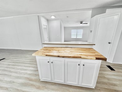 Kitchen with butcher block countertops, light wood-style flooring, ceiling fan, and white cabinetry