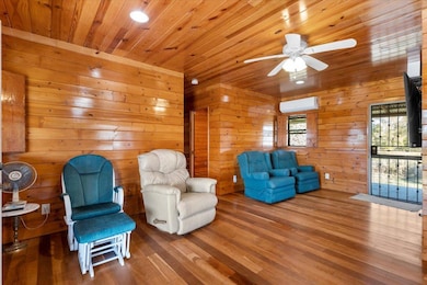 Living area featuring wood finished floors, wood ceiling, wood walls, a ceiling fan, and a wall unit AC