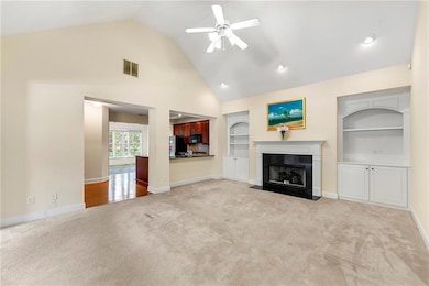 Unfurnished living room with light colored carpet, ceiling fan, built in shelves, a high end fireplace, and baseboards