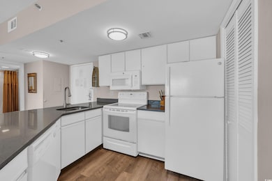 Kitchen with white appliances, dark countertops, dark wood-style floors, and white cabinetry