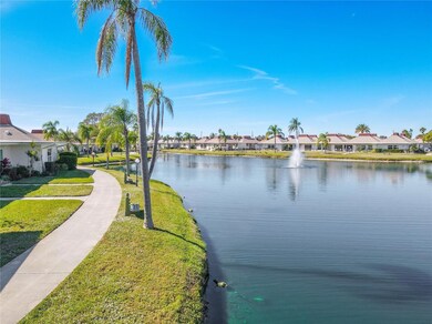 Scenic walking path winding around a serene, palm-lined pond with a beautiful fountain as the focal point in the background. The pathway offers a peaceful setting for leisurely strolls, surrounded by lush landscaping and tranquil water views.