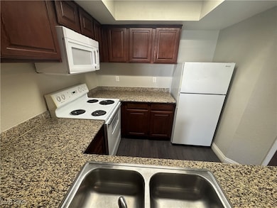 Kitchen with white appliances, a sink, and dark wo