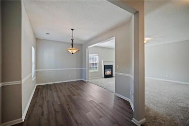Unfurnished dining area with a textured ceiling, wood finished floors, baseboards, and a glass covered fireplace