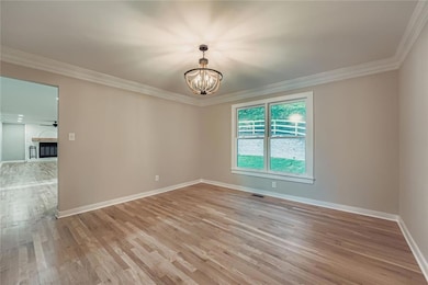 Unfurnished room with light wood-type flooring, crown molding, a fireplace, a chandelier, and ceiling fan
