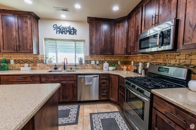 Kitchen featuring appliances with stainless steel finishes, backsplash, dark brown cabinetry, light stone counters, and light tile patterned flooring