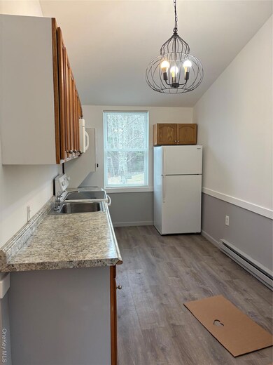Kitchen featuring brown cabinetry, a baseboard radiator, refrigerator, light wood finished floors, and light countertops