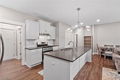 Alternate view of the kitchen featuring kitchen island with sink, subway tile backsplash, white cabinets, luxury vinyl plank floors, stainless steel gas range oven, and quartz countertops.