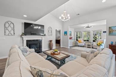 Living area with a chandelier, wood finished floors, a glass covered fireplace, recessed lighting, and vaulted ceiling