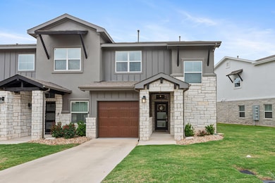 View of front of home with board and batten siding, stone siding, an attached garage, driveway, and a front lawn