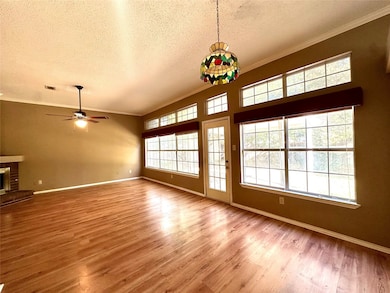 Unfurnished living room with crown molding, a textured ceiling, light wood-type flooring, a ceiling fan, and a fireplace