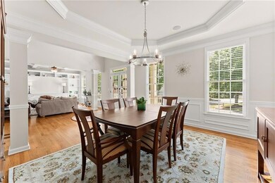 Dining space featuring ornate columns, a tray ceiling, a wainscoted wall, light wood-style flooring, and ornamental molding