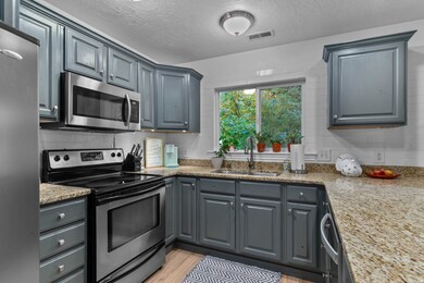 Kitchen featuring appliances with stainless steel finishes, gray cabinetry, a textured ceiling, light stone counters, and light wood-style floors