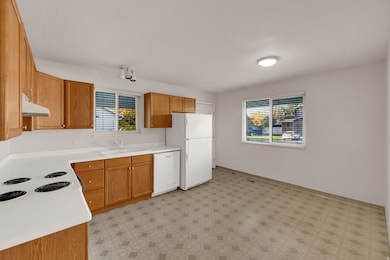 Kitchen featuring brown cabinets, light countertops, white appliances, light floors, and under cabinet range hood