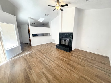 Unfurnished living room featuring a brick fireplace, wood finished floors, a ceiling fan, a textured ceiling, and high vaulted ceiling