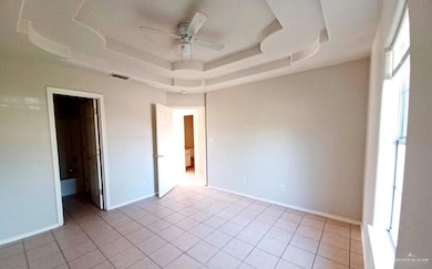 Unfurnished bedroom featuring a raised ceiling, light tile patterned floors, and ceiling fan